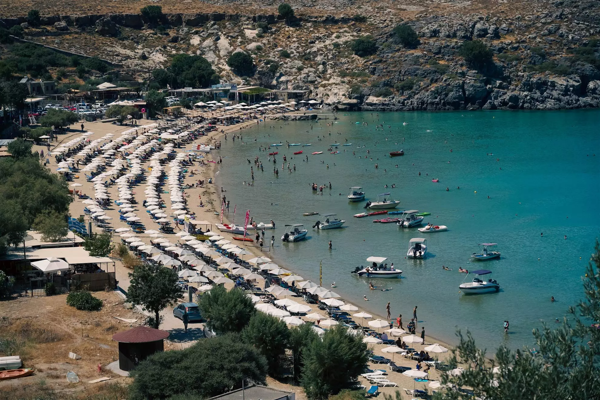 Vista di una spiaggia assolata con stabilimenti balneari, ombrelloni, villeggianti, natanti e piccoli yatch.