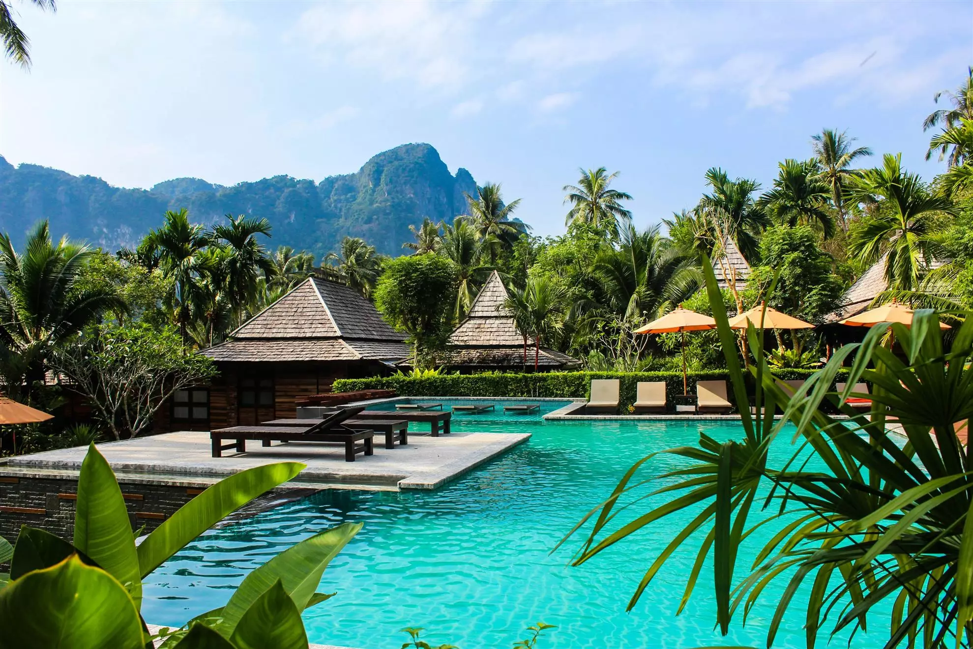 Piscina di un resort caraibico circondata da vegetazione lussureggiante e montagne sullo sfondo, creando un'atmosfera tranquilla e naturale.