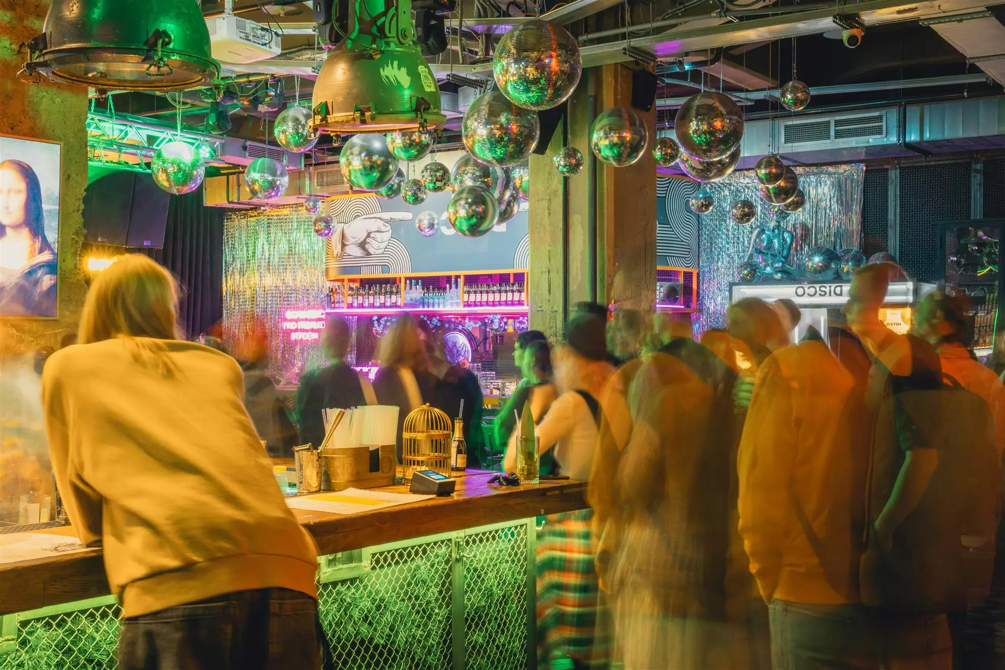 Persone in piedi in un discopub affollato, immerse in conversazioni e nell'atmosfera animata del locale.