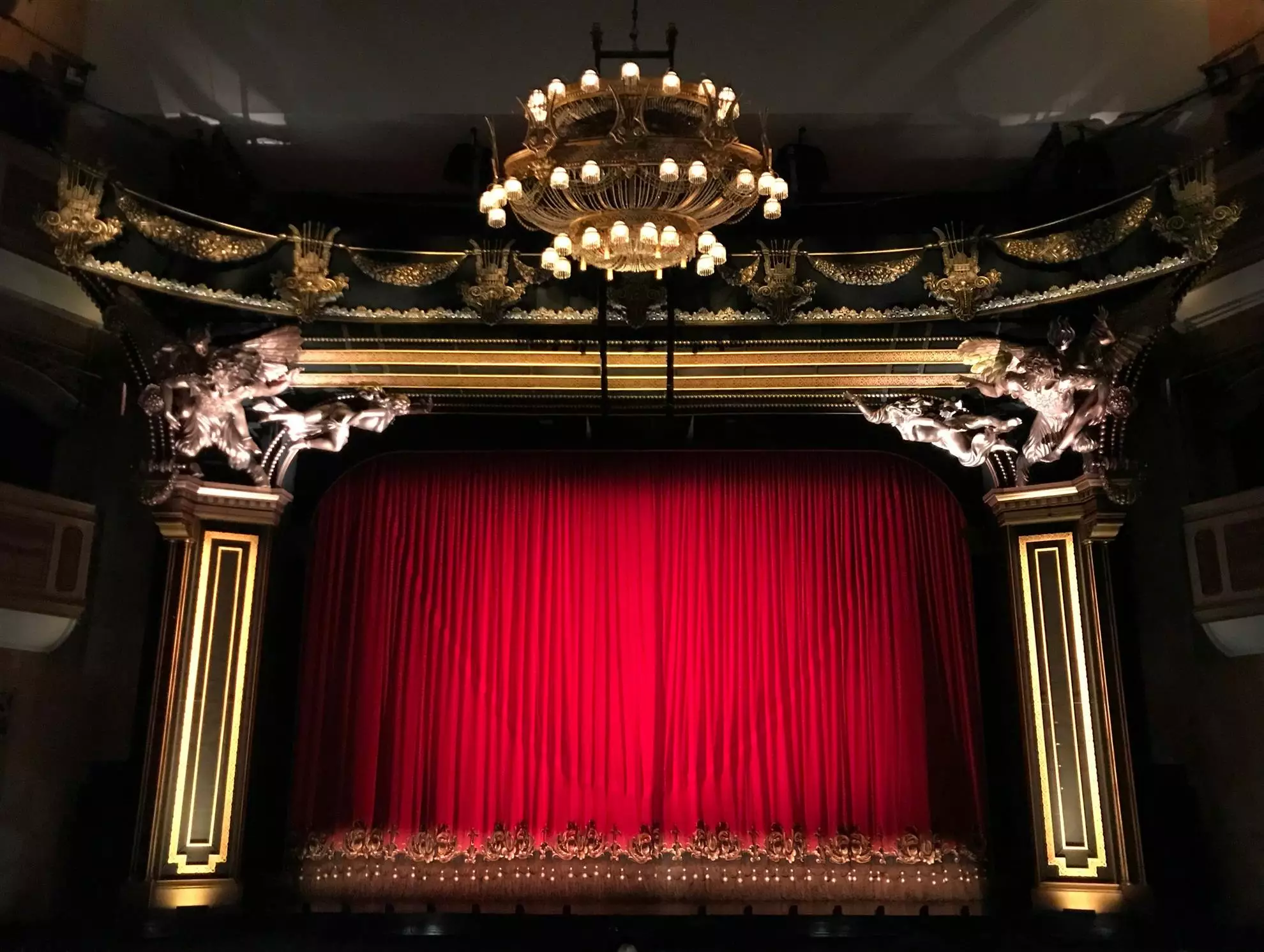 Vista del palcoscenico di un teatro, con architettura storica e pubblico in attesa di uno spettacolo.