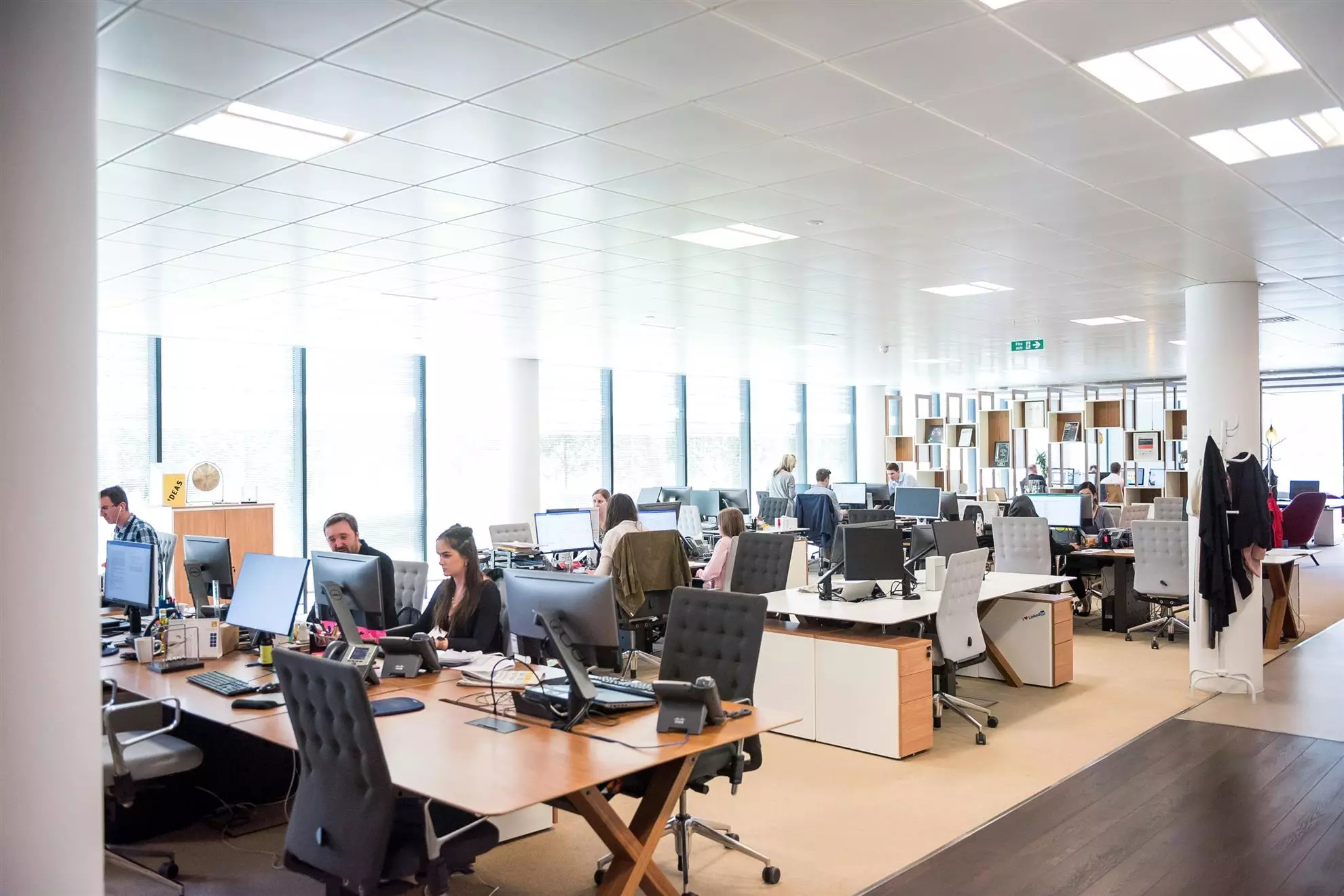 Ufficio con persone che lavorano a scrivanie, circondate da computer e materiali di lavoro. 