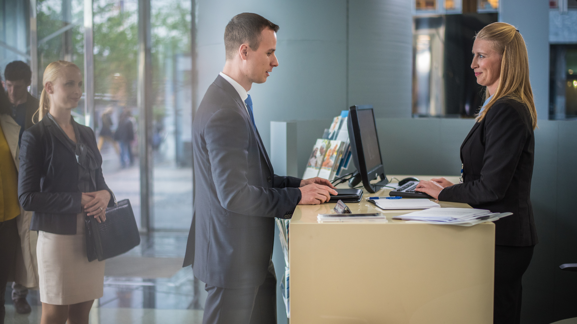 Un uomo e una donna attorno a una scrivania di una banca, intenti a lavorare davanti a un computer. 
