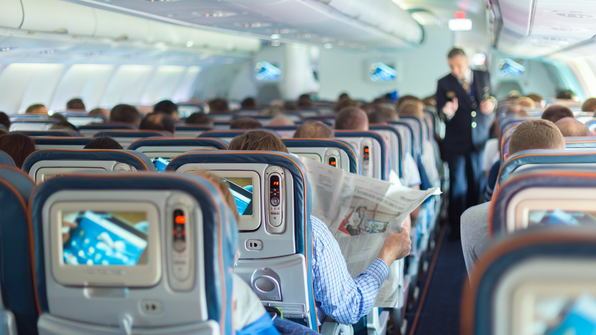 Gruppo di passeggeri su un aereo, alcuni indossano cuffie, altri sono impegnati in attività diverse durante il viaggio.