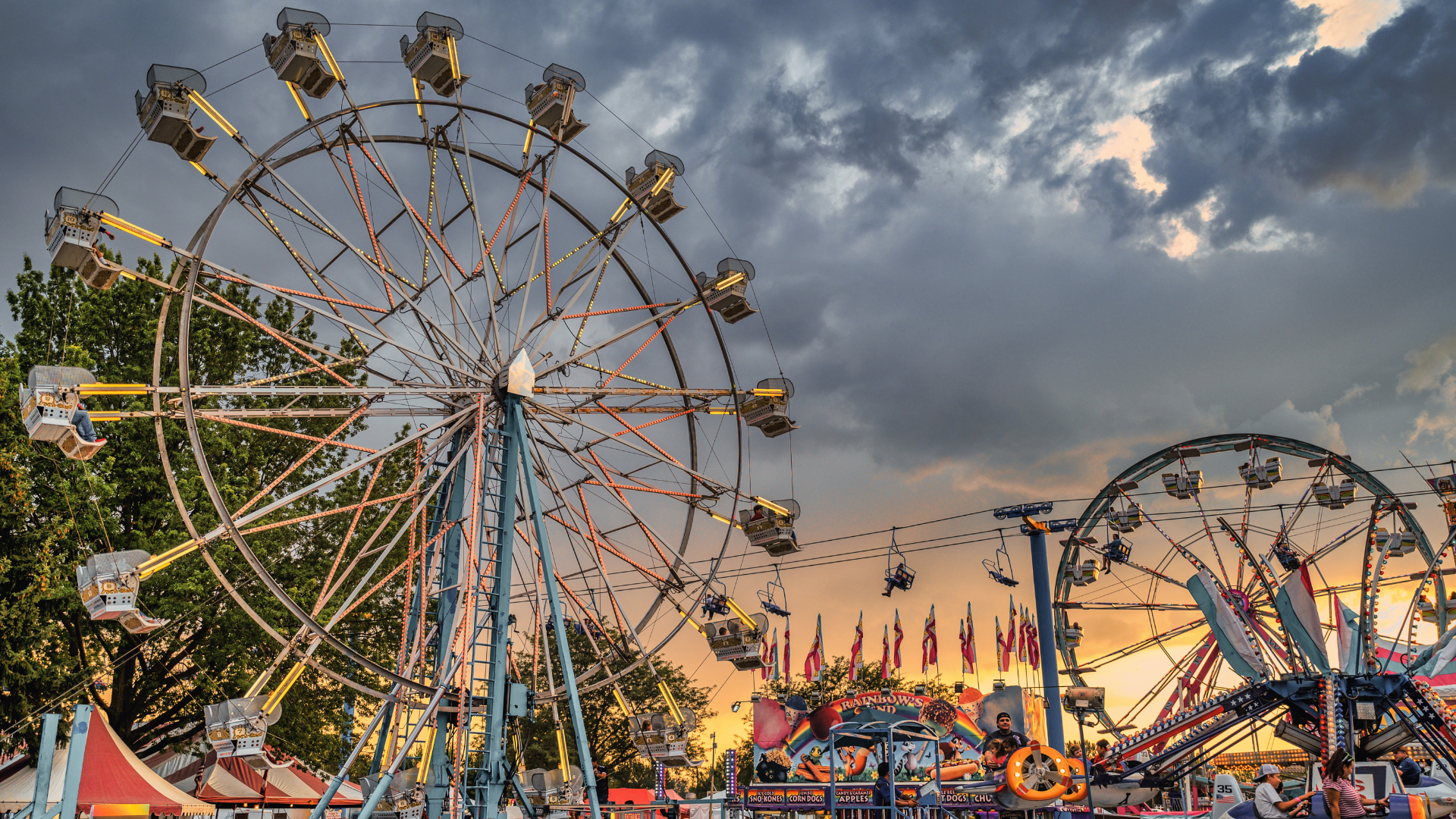 Vista di una ruota panoramica e giostre in un parco divertimento, con luci brillanti e persone che si godono l'evento.