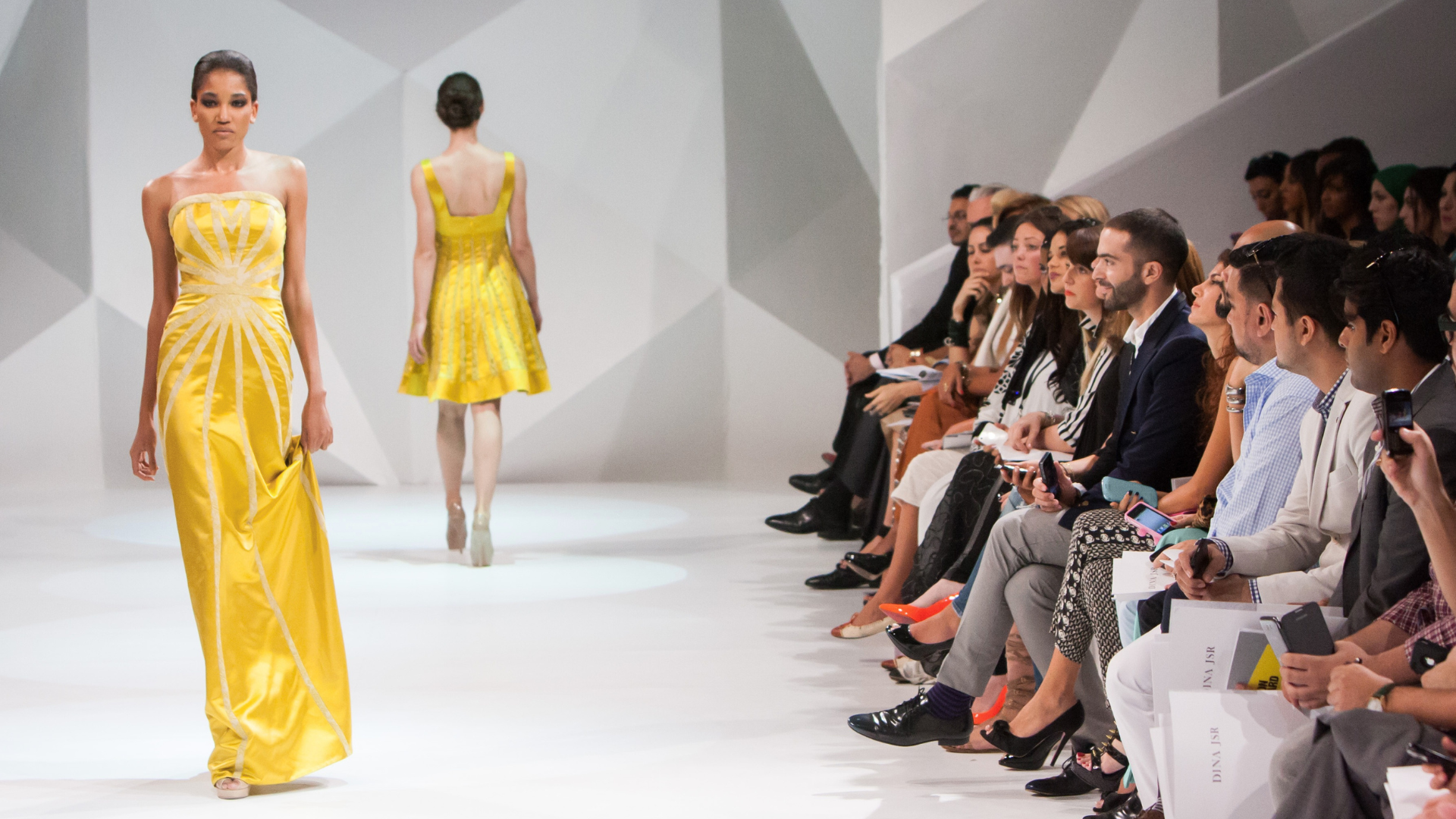 Sfilata di moda: una donna indossa un vestito giallo mentre percorre la passerella con sicurezza.